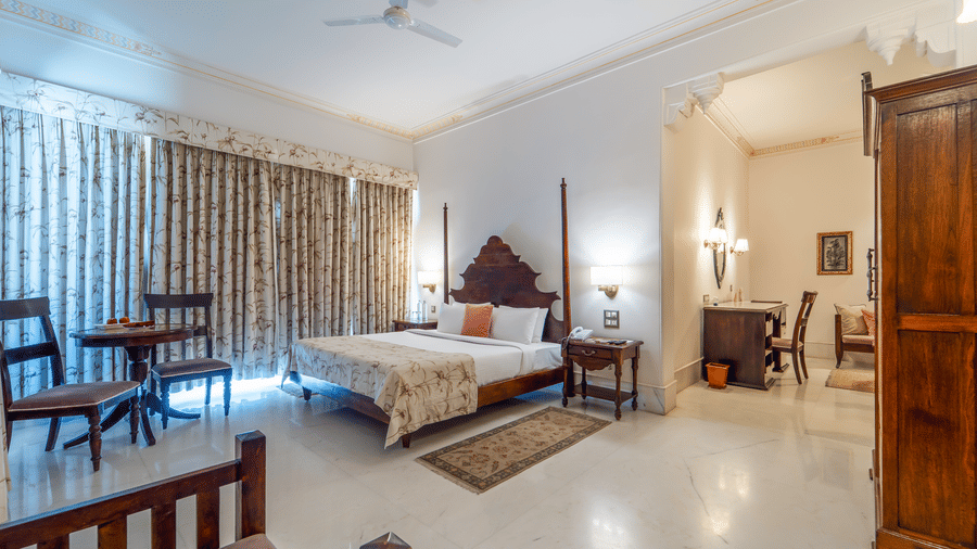A classic guest room featuring a dark wood 2-poster bed, marble floors, and traditional arched doorways - Fateh Garh, Udaipur