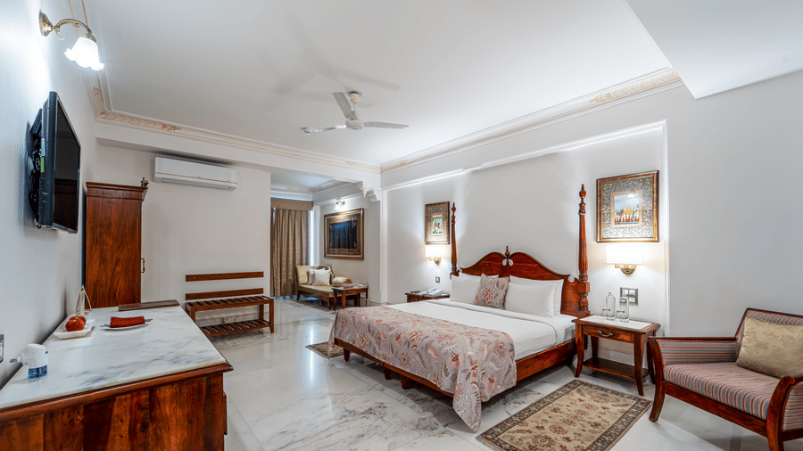 A wide interior shot of a luxury suite showing a large bed, wooden furniture, and a seating area - Fateh Garh, Udaipur