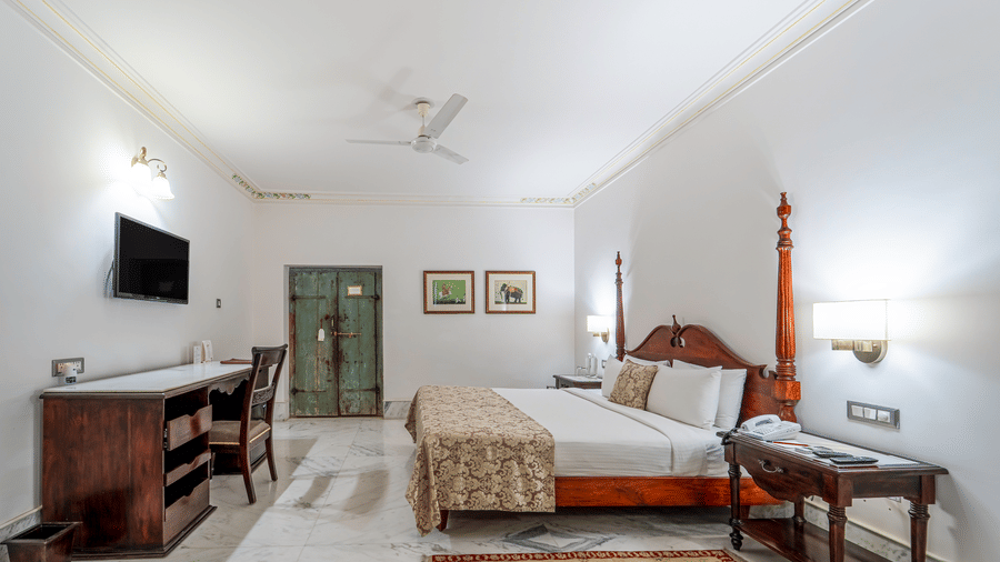 A heritage-style bedroom featuring a dark wood desk, a four-poster bed, and warm ambient lighting - Fateh Garh, Udaipur