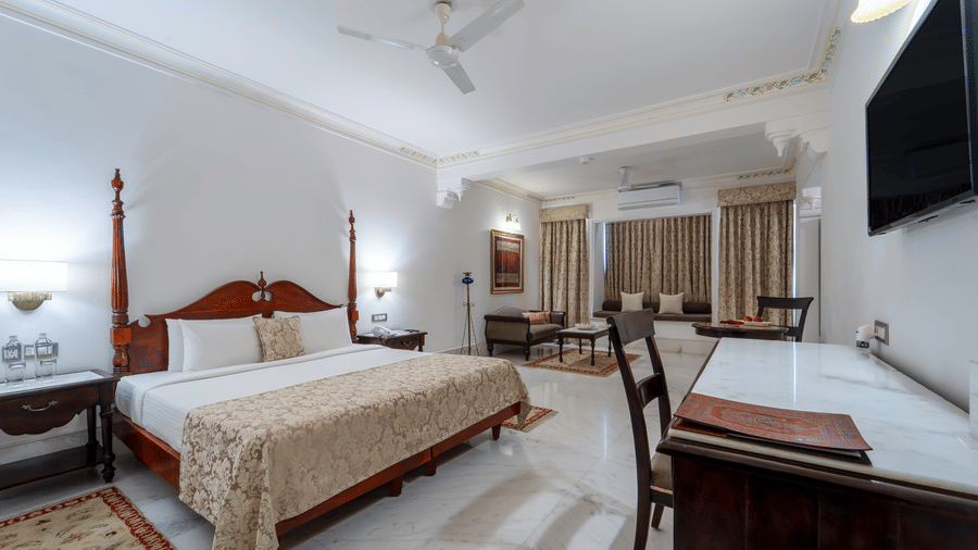 A view of a grand bedroom showing the television area, a work desk, and a large bed with floral linens - Fateh Garh, Udaipur