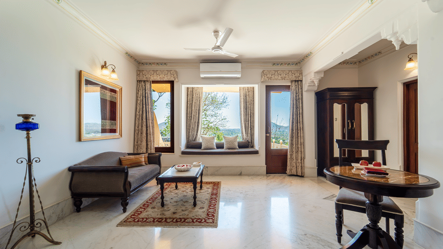 A formal living area within a suite featuring a dark sofa, a small dining table, and large windows with scenic views - Fateh Garh, Udaipur