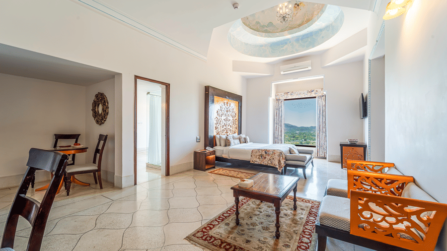 A wide-angle view of a bright luxury suite featuring marble floors, carved wooden furniture, and scenic window views - Fateh Garh, Udaipur