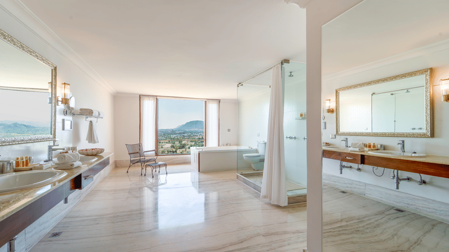 A spacious white marble bathroom featuring a double vanity and a soaking tub positioned next to a view window - Fateh Garh, Udaipur