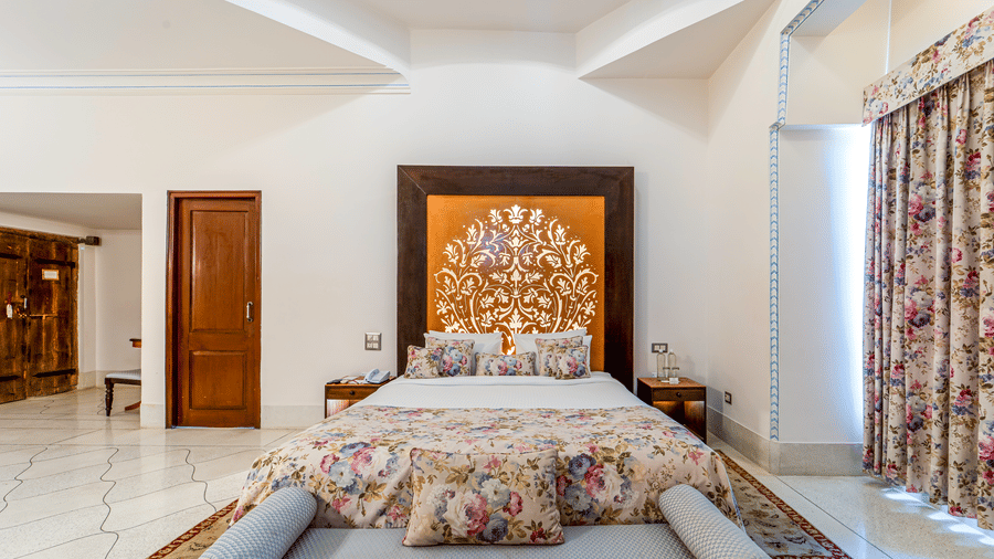 A luxury bed setup with an intricately carved golden headboard and traditional architectural details - Fateh Garh, Udaipur