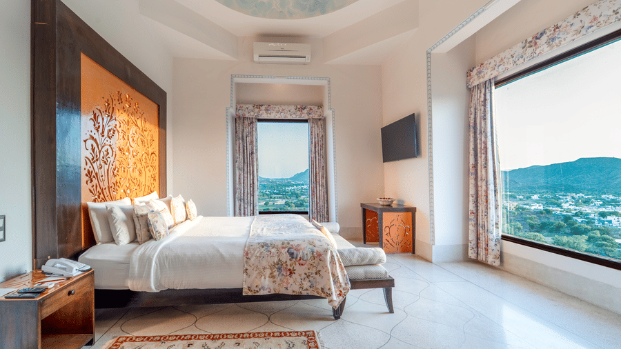 A grand bedroom with a king size bed, ornate headboard, and a large window overlooking the Aravalli hills - Fateh Garh, Udaipur