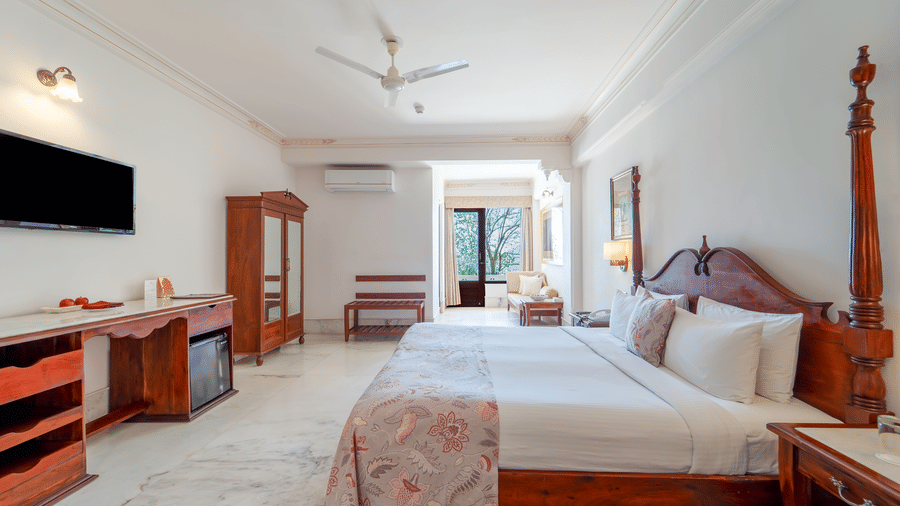 A wide view of a grand suite featuring a king size bed, dark wood furniture, and a wall-mounted television - Fateh Garh, Udaipur