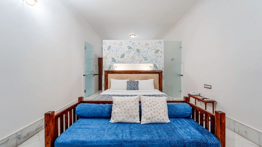A clean, minimalist bedroom featuring a blue velvet bench at the foot of a plush bed - Fateh Garh, Udaipur