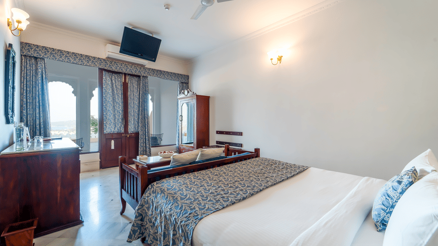 A well-appointed guest room with a double bed and glass windows leading to a private balcony - Fateh Garh, Udaipur