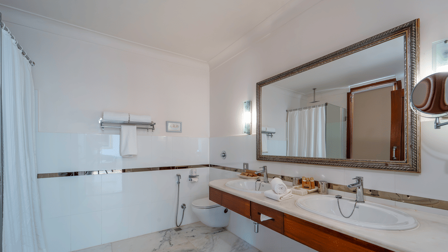 A bright bathroom interior with polished marble walls, a large wooden vanity with an inset sink, and a framed mirror - Fateh Garh, Udaipur