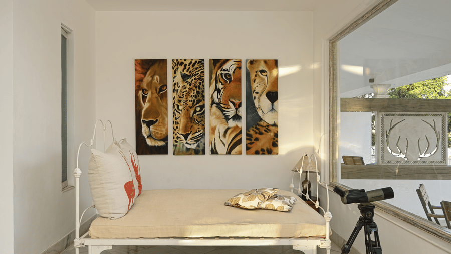 A bed at Fateh Safari Resort, Kumbhalgarh featuring pillows and cushions placed on it and binoculars mounted on a tripod aimed towards the window.