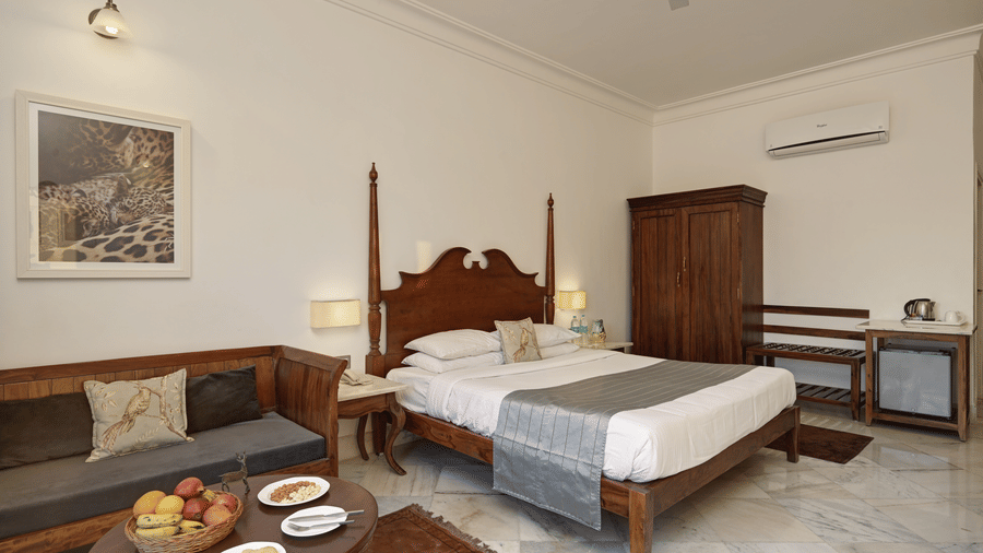 Deluxe Room with Balcony at Fateh Safari Resort, Kumbhalgarh featuring a double size bed, a sofa with centre table, a wardrobe, a cabinet table, and an air-conditioner.