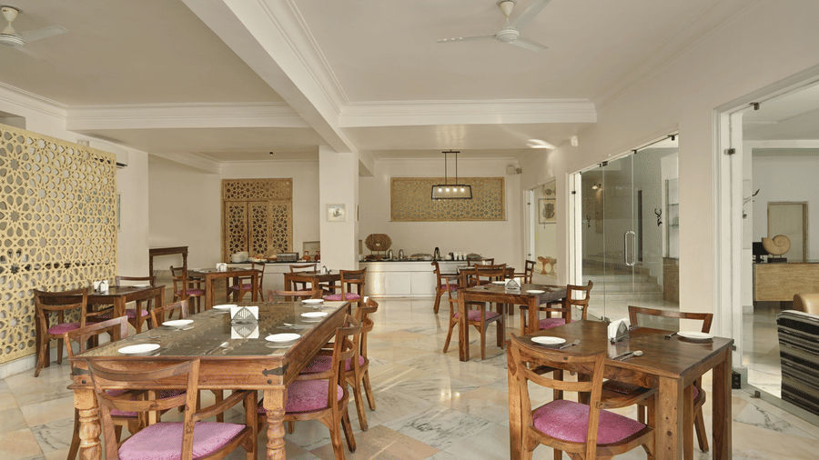Lobby restaurant at Fateh Safari Resort, Kumbhalgarh featuring tables and chairs and a kitchen counter with plates, cutlery, bowls, jugs, etc.
