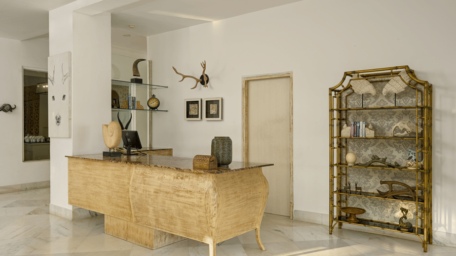 Reception at Fateh Safari Resort, Kumbhalgarh featuring wooden desk, a computer placed on it with other decorative items, and a shelve with all the antique pieces.  