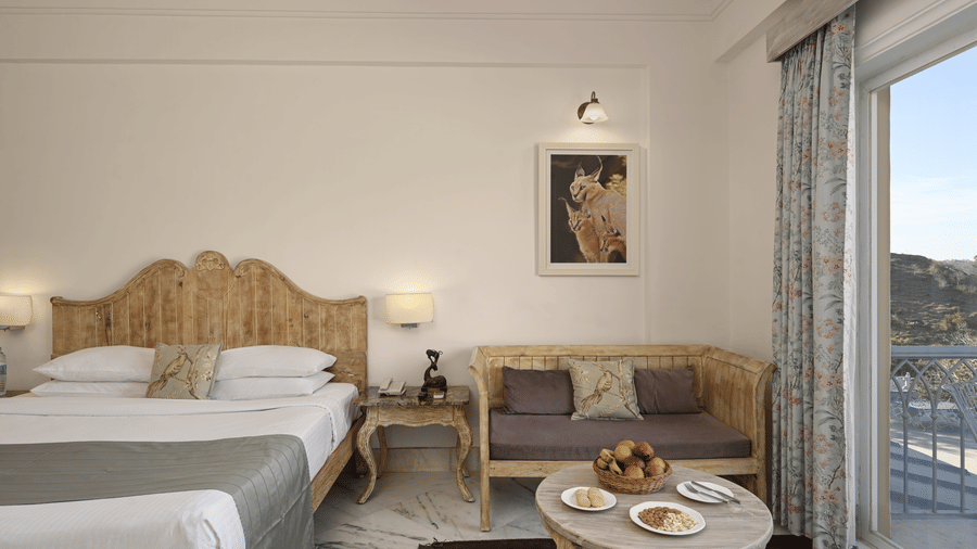 Superior Room with Balcony at Fateh Safari Resort, Kumbhalgarh featuring a double size bed, bedside tables with lamps on either side, a sofa with centre table, and an attached balcony.