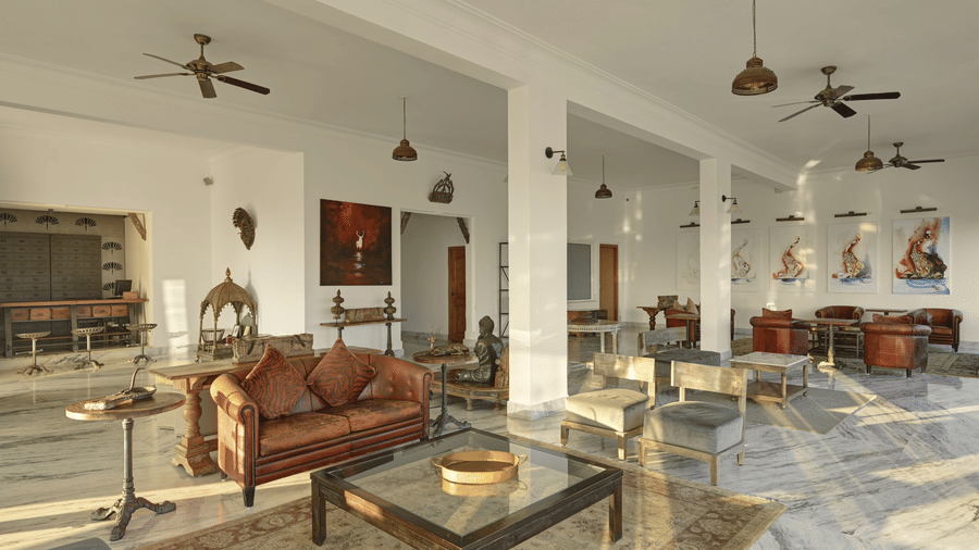 A lobby at Fateh Safari Suites, Kumbhalgarh featuring sofa sets, stools, centre table, and several antique and decorative pieces.