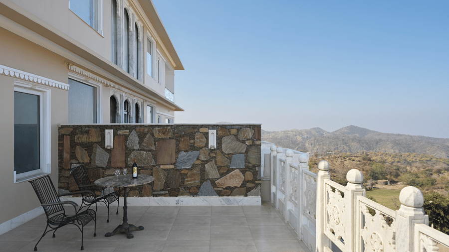 Balcony of Plunge Pool Suite in Fateh Safari Suites featuring two chairs and a table where a bottle of wine and two glasses are kept. 