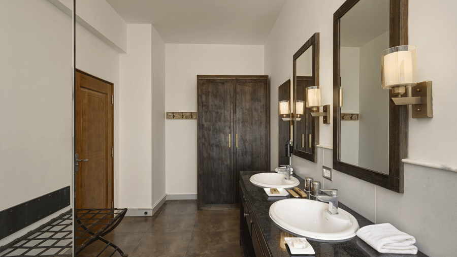 Bathroom of Plunge Pool Suite in Fateh Safari Suites featuring sink and faucet, mirrors on the walls with electric lamps, and a wardrobe.