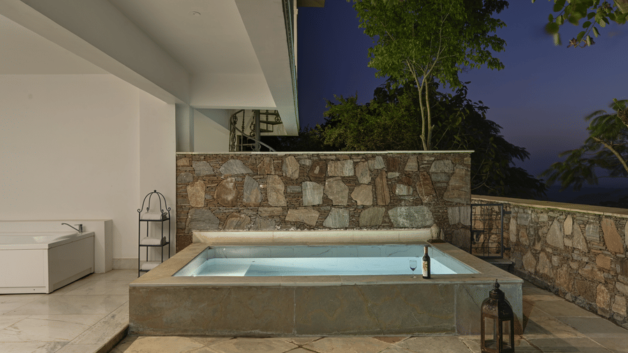 Plunge Pool Suite with Jacuzzi at Fateh Safari Suites, Kumbhalgarh featuring a small pool, a towel rack next to it, a bottle of wine in open area where night sky is visible.