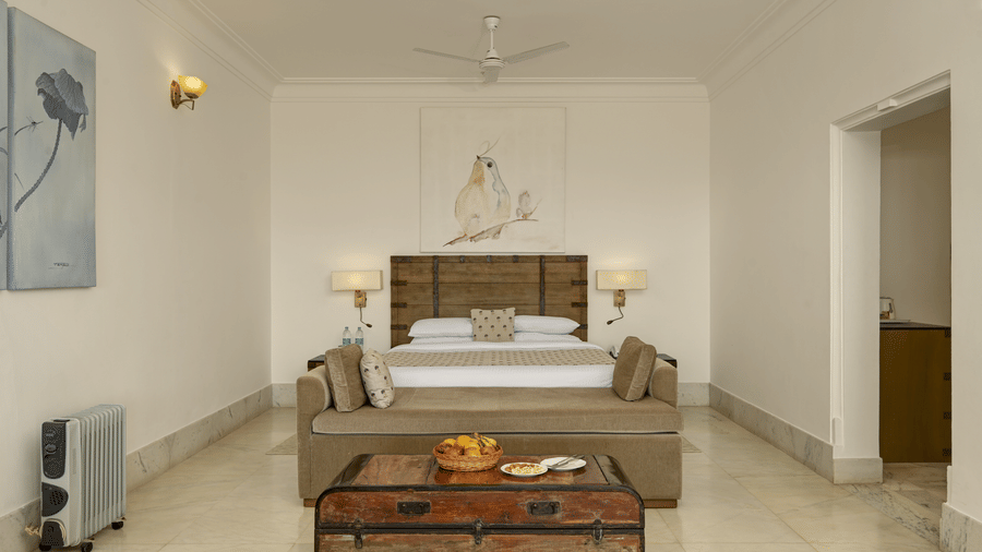 Plunge Pool Suite with Jacuzzi at Fateh Safari Suites, Kumbhalgarh featuring a bed, lamps and bedside tables on either side, a sofa at the centre, and a table where fruits and other foods are kept. 