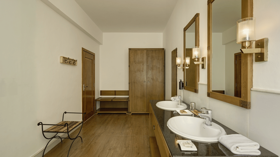 Bathroom of Plunge Pool Suite with Jacuzzi at Fateh Safari Suites, Kumbhalgarh featuring two sinks, with faucets and mirror attached on the wall,  other toiletries and a wardrobe at one corner.