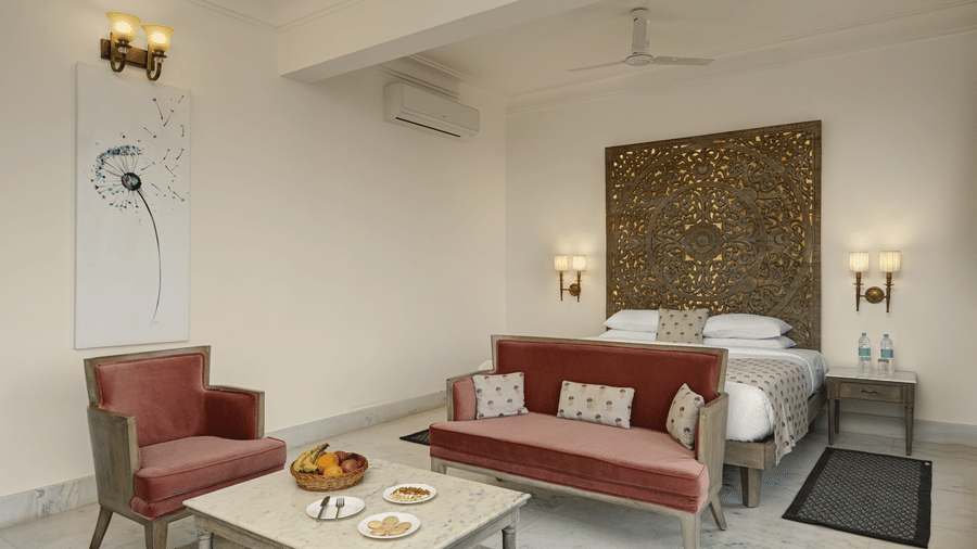 Seating area in Plunge Pool Suite with Jacuzzi at Fateh Safari Suites, Kumbhalgarh featuring sofa set and centre table. Behind it there is a bed and few electric lamps turned on in the room.