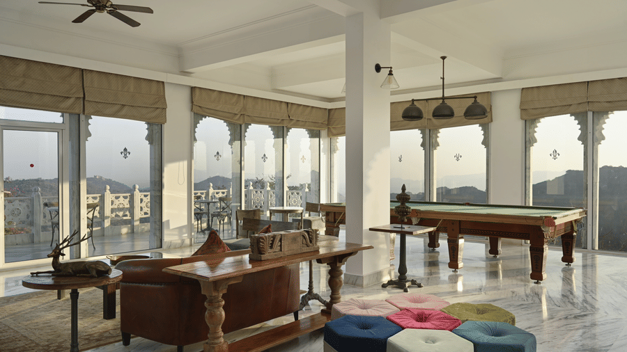 A reception area at Fateh Safari Suites, Kumbhalgarh featuring seating area with sofas, stools, a pool table, and open walls which provides view of the world outdoor.