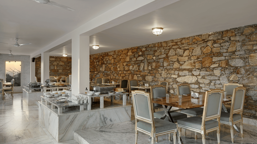 A restaurant at Fateh Safari Suites, Kumbhalgarh featuring sets of tables and chairs and food counters
