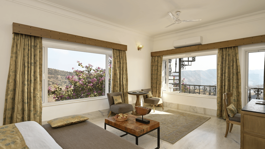 Valley View Suite with Jacuzzi at Fateh Safari Suites, Kumbhalgarh large windows which has filled the room with natural light. The room features sofa bench, sofa chairs, centre table, and a bed.