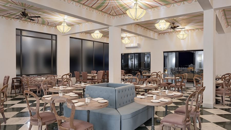 Fateh Vilas Udaipur - interior view of the restaurant featuring wooden chairs and tables on a black and white chequered tiles