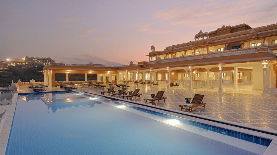 Facade of Fateh Vilas in Udaipur featuring a well lit building and a swimming pool.