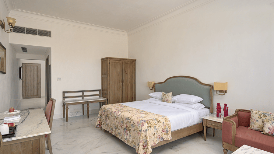 A room at Fateh Vilas, Udaipur, featuring a king size bed a wardrobe seating options and white ceiling fan