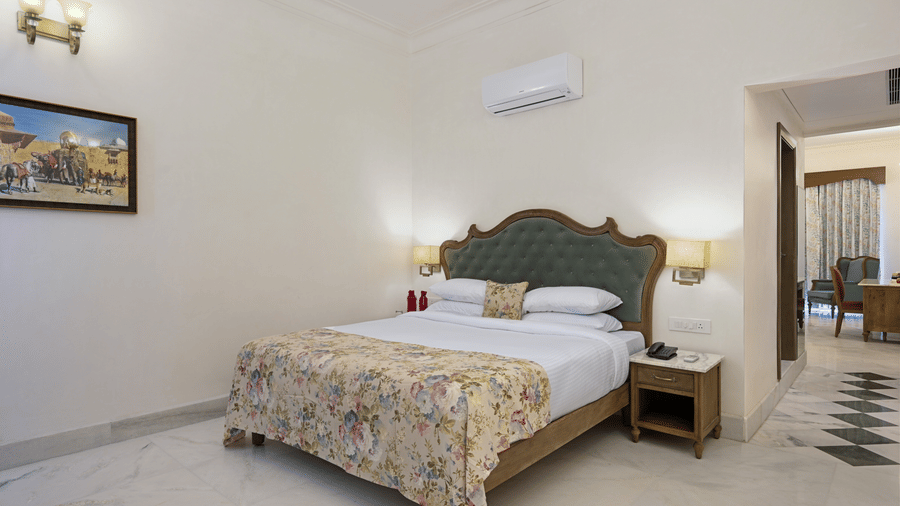 Interior view of the Family Plunge Pool Suite in Udaipur at Fateh Vilas, featuring a king size bed, an air conditioner overhead and lamps on both sides over the nightstands