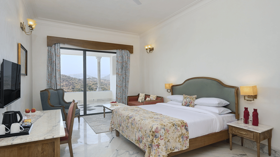 Family Suite in Udaipur with a sit-out at Fateh Vilas, featuring a king size bed with lamps on both sides facing the TV and a doorway to the balcony