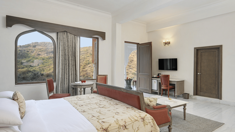 A suite at Fateh Vilas, Udaipur, featuring a king size bed a work desk a television and windows with curtains