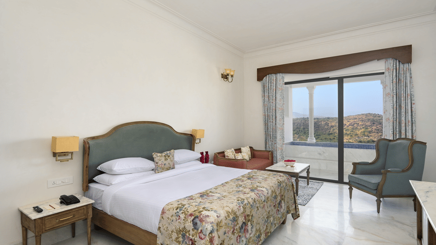 Interior view of the Plunge Pool Suite featuring a queen size bed, with side tables, lamps, a chair and a floor to ceiling sliding door to reach the plunge pool, offering the finest accommodation in Udaipur