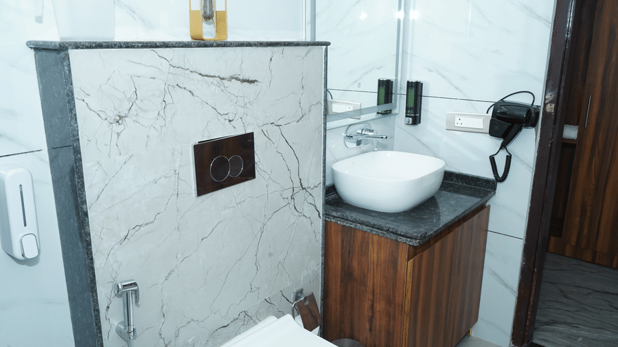 Close-up of guest bathroom vanity showing a white counter top basin sink, dark wood cabinet, wall-mounted hair dryer, and soap dispenser - Five Elements Hotels, Corbett Crown Resort, Jim Corbett