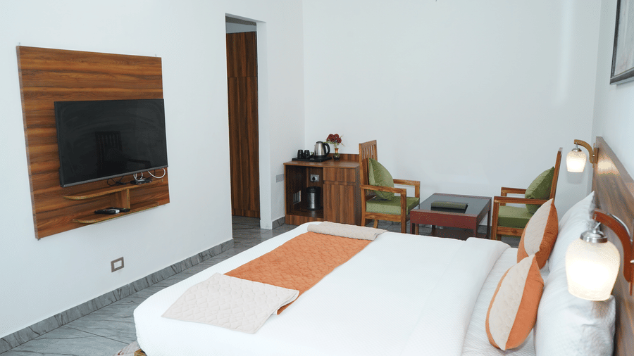 Spacious guest bedroom view showing a double bed, wall-mounted flat-screen television, tea setup, and wooden seating area - Five Elements Hotels, Corbett Crown Resort, Jim Corbett