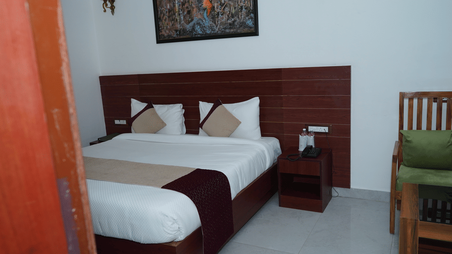 View entering a deluxe guest room with a double bed, dark wooden headboard panel, nightstands, and wall artwork - Five Elements Hotels, Corbett Crown Resort, Jim Corbett