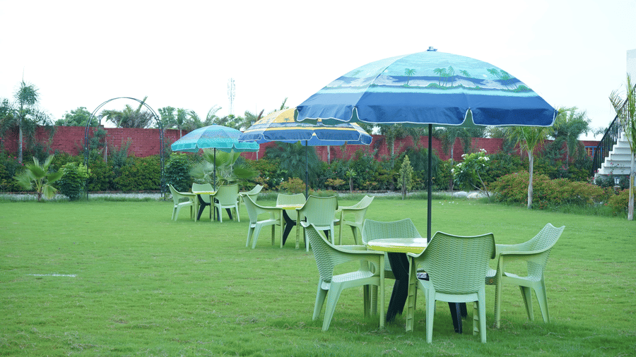 Close-up of outdoor lawn seating featuring light green plastic chairs paired with dark blue shade umbrellas on a bright green garden lawn - Five Elements Hotels, Corbett Crown Resort, Jim Corbett