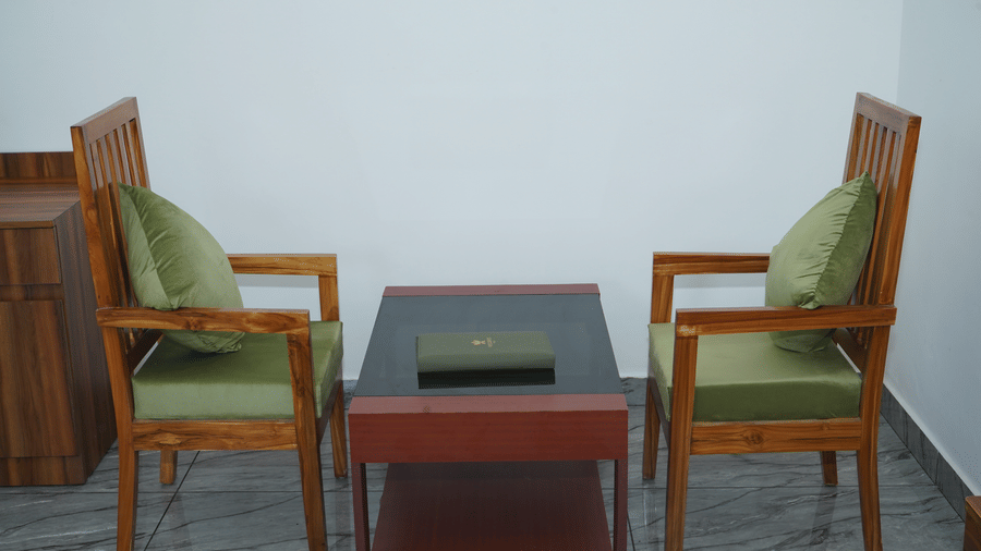 Private room seating setup featuring 2 tall wooden armchairs with green cushions facing a small wooden center table - Five Elements Hotels, Corbett Crown Resort, Jim Corbett