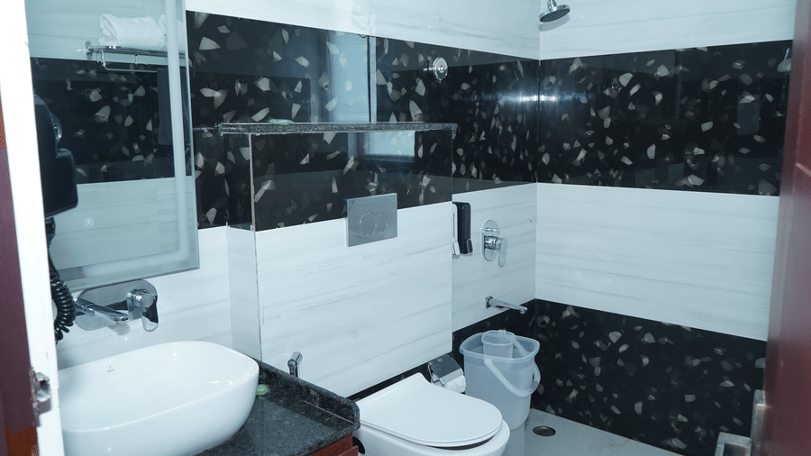 Clean modern resort bathroom featuring black and white tiled walls, a white porcelain counter sink, wall-mounted toilet, and shower area - Five Elements Hotels, Corbett Crown Resort, Jim Corbett