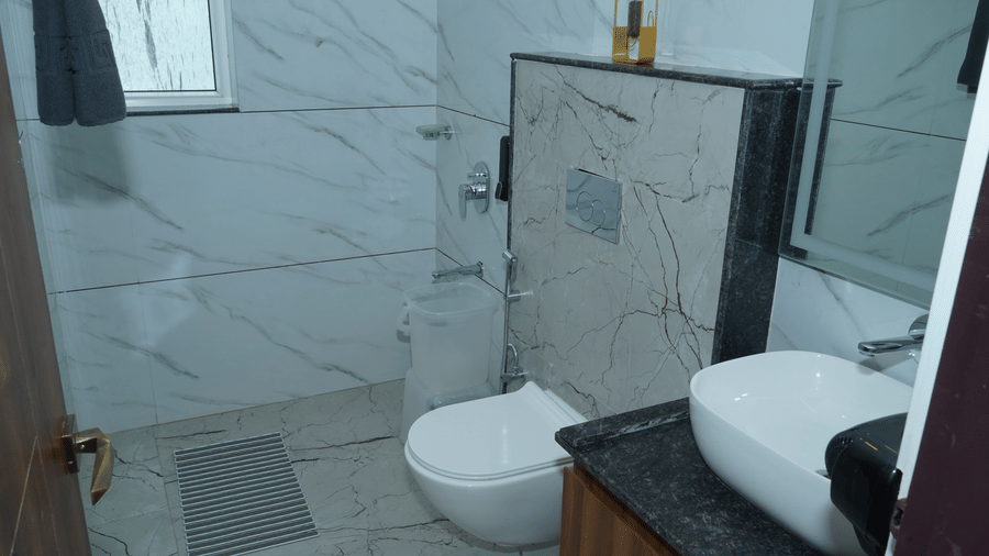 Modern en-suite resort bathroom featuring white marble tile walls, a ceramic vessel sink, a wall-hung toilet, and ambient lighting - Five Elements Hotels, Corbett Crown Resort, Jim Corbett