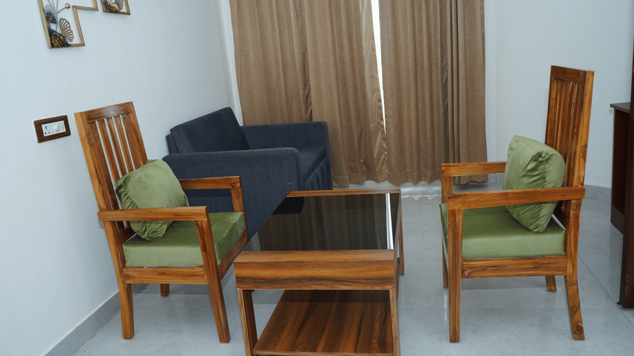 Seating corner inside a resort room with two high-back wooden armchairs with green cushions, a coffee table, and a plush sofa set - Five Elements Hotels, Corbett Crown Resort, Jim Corbett