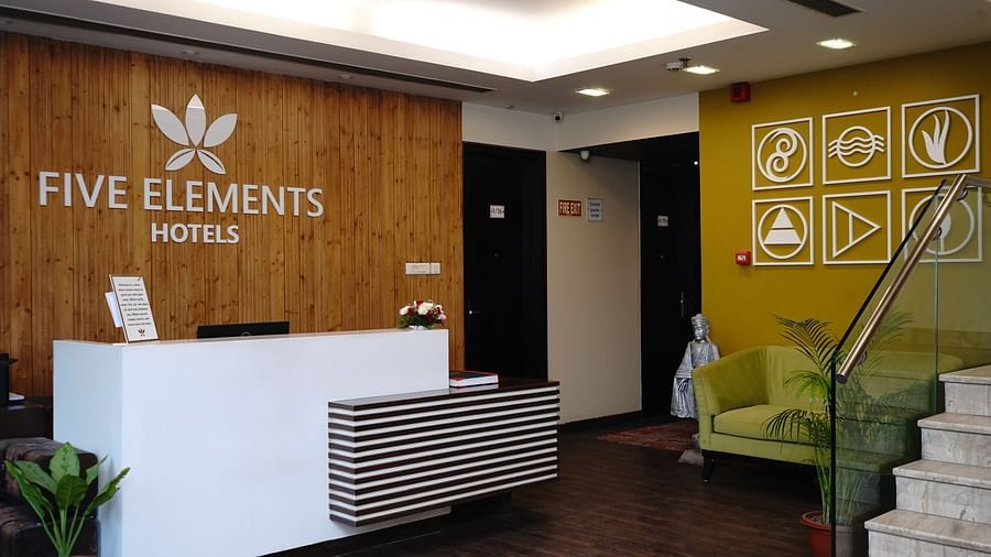 An image of a reception lobby at Five Elements Hotels North Avenue, Delhi featuring a reception desk, a sofa, and a staircase next to it