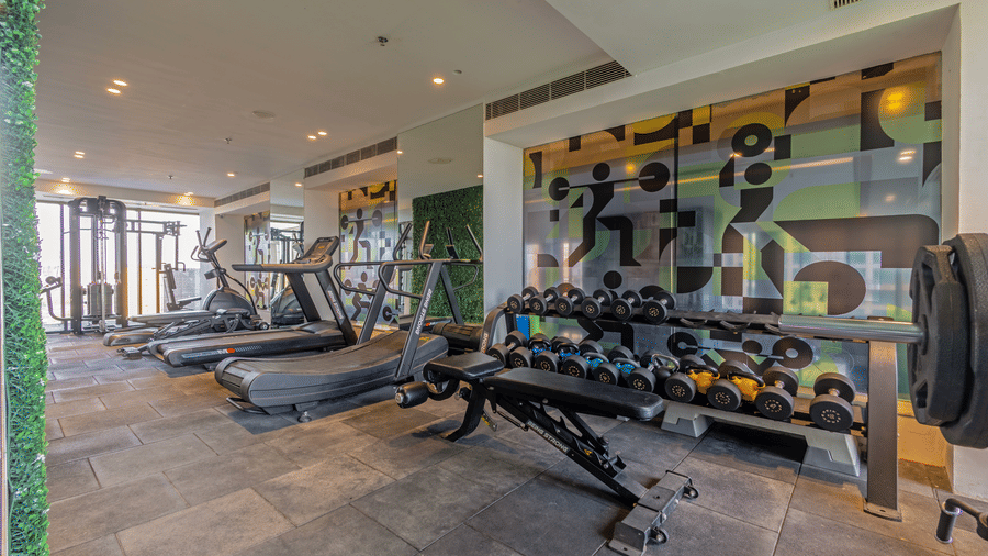 Indoor gym setup featuring weight benches, a dumbbell rack, and treadmills at Golden Tulip - Sector 80, Gurugram.
