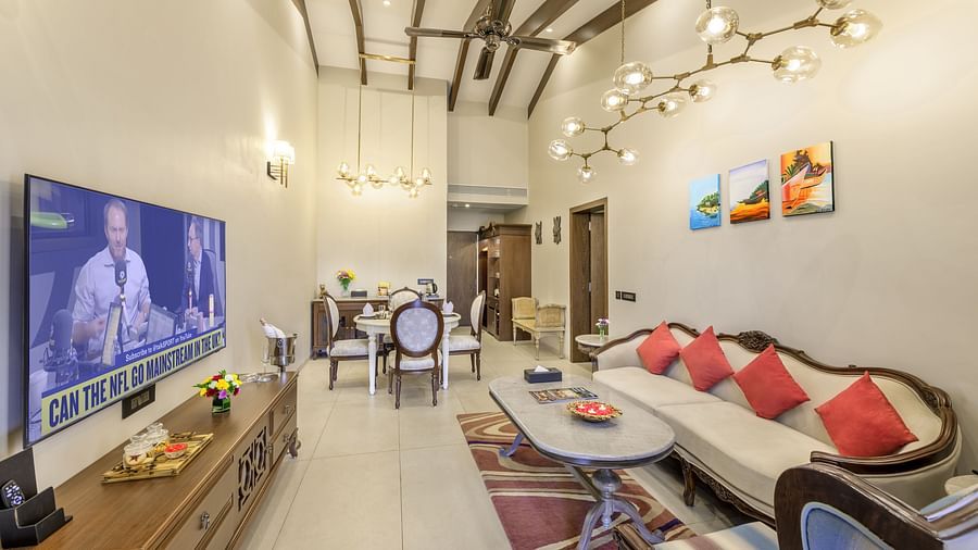 the living area of our suite in candolim featuring a love seat with coffee table, a wall-mounted television, high ceilings, and an attached dining area - Golden Tulip, Candolim, Goa