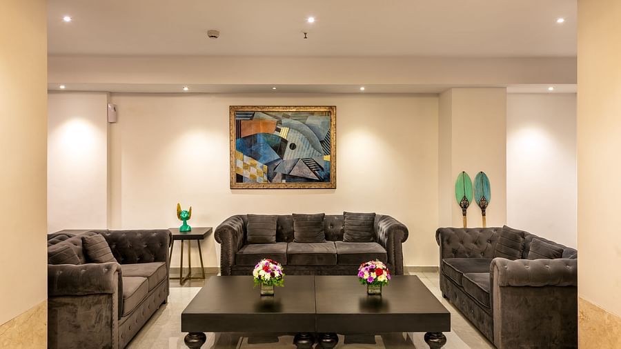 a wide angle view of the waiting area in our lobby featuring three black leather couches and a coffee table - Golden Tulip, Candolim, Goa