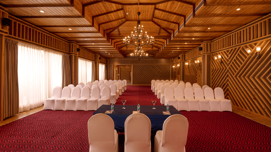 Empty banquet hall with wood-panelled walls, a sculpted ceiling with cove lighting, arched glass double doors, and a glossy tiled floor throughout.