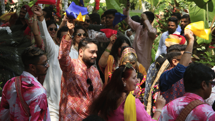 Wedding guests in festive Indian attire waving colorful scarves during a baraat celebration amid tropical foliage at Golden Tulip Goa, Mandrem Beach.