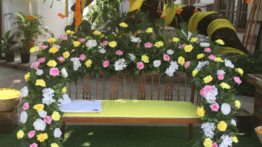 Wooden bench with a yellow seat framed by an arch of pink, yellow, and white flowers under a garlanded tree at Golden Tulip Goa, Mandrem Beach.